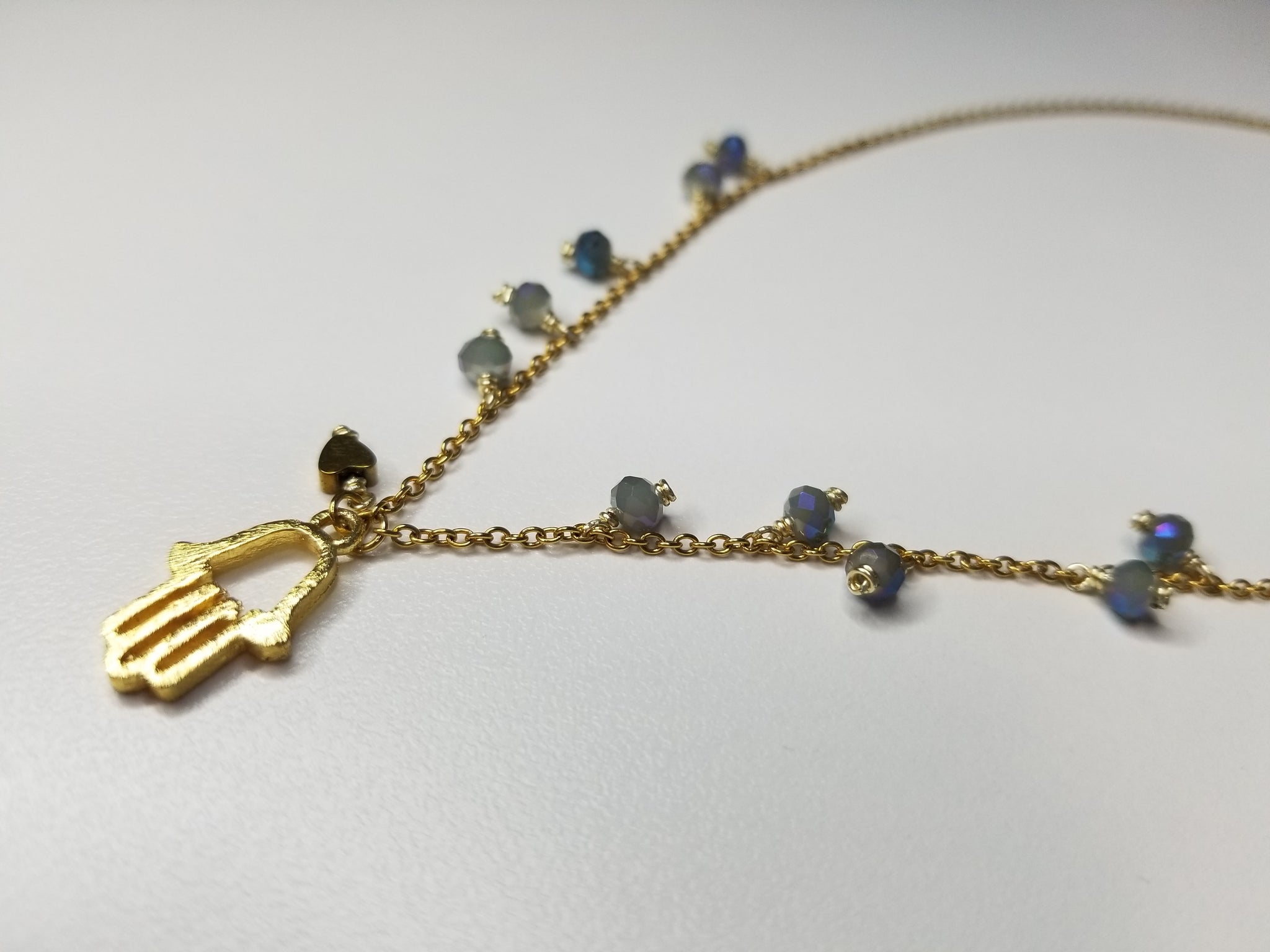 Gold metal necklace with light blue beads and Hamsa.